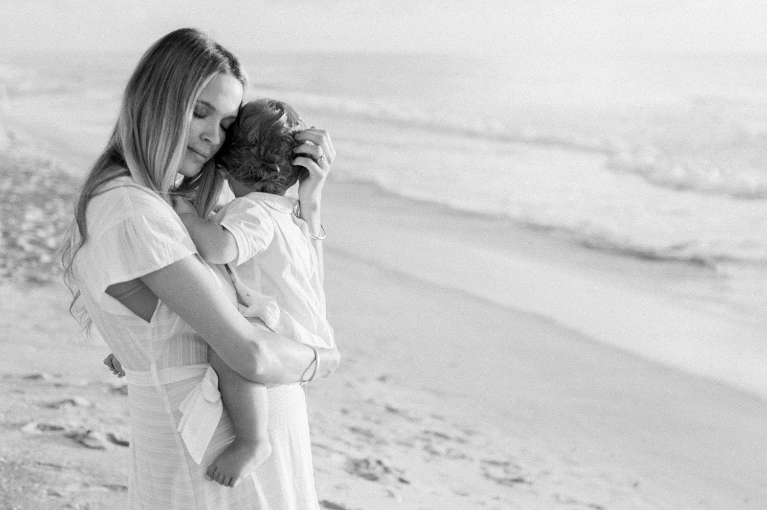 black and white image of mother embracing her little boy along the coast