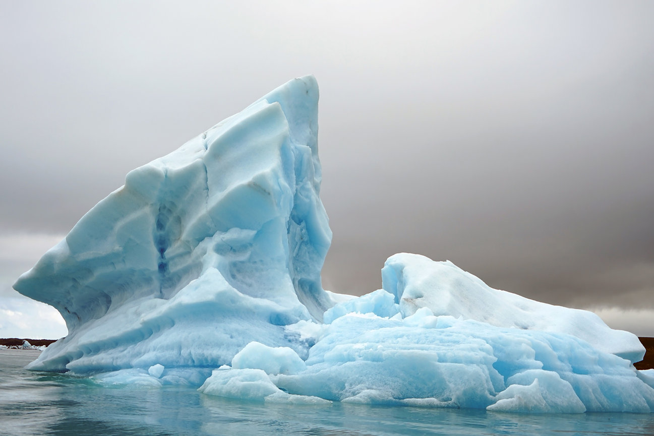Large blue iceberg floating in calm water under a cloudy sky