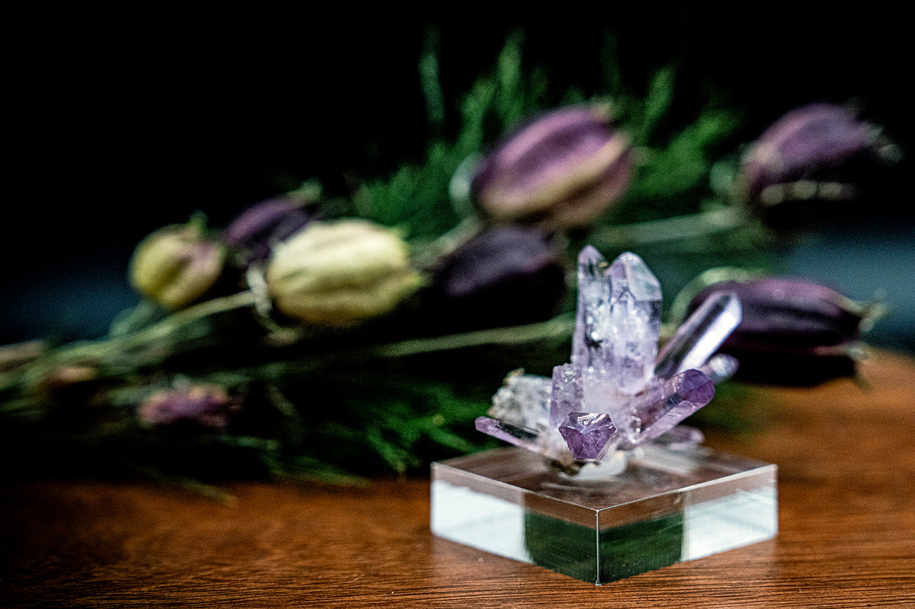 Purple crystal sculpture on a clear block with blurred flowers in the background