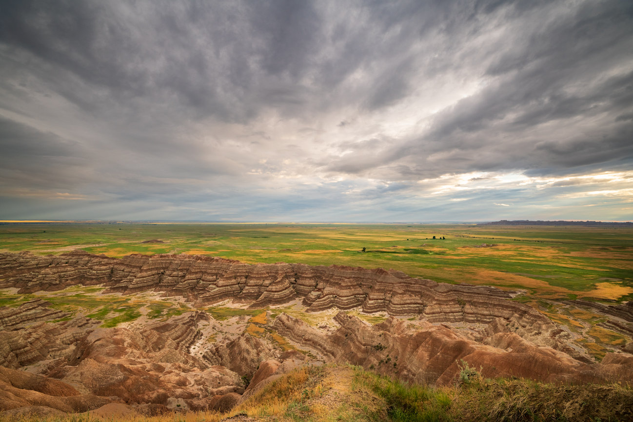Eroded hills and open plains stretch beneath a dramatic cloudy sky.