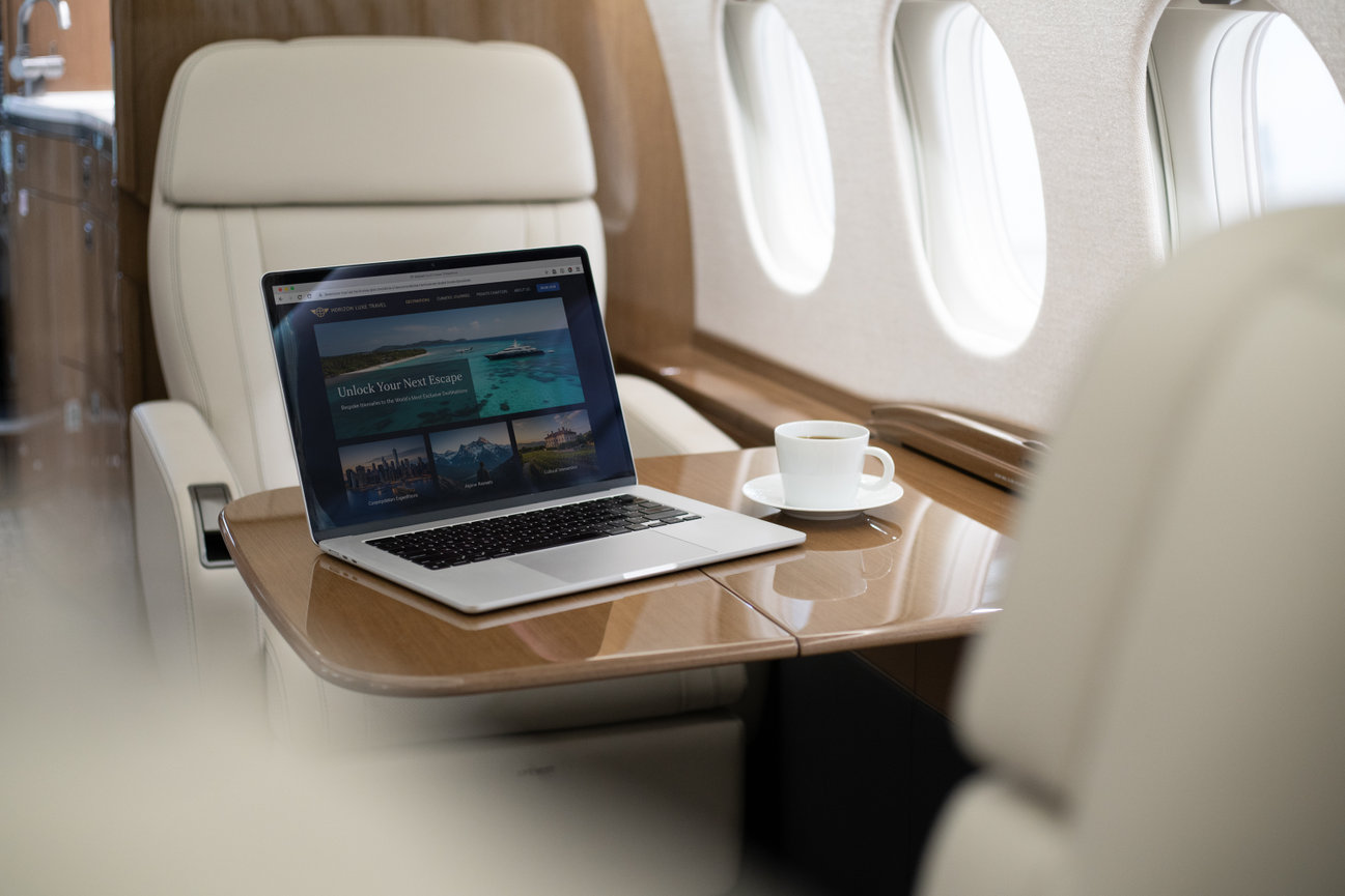 Laptop and coffee on a table in a private jet cabin with beige leather seating.