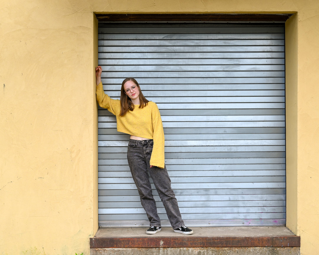 Young woman in a yellow sweater leaning against a metal shutter door