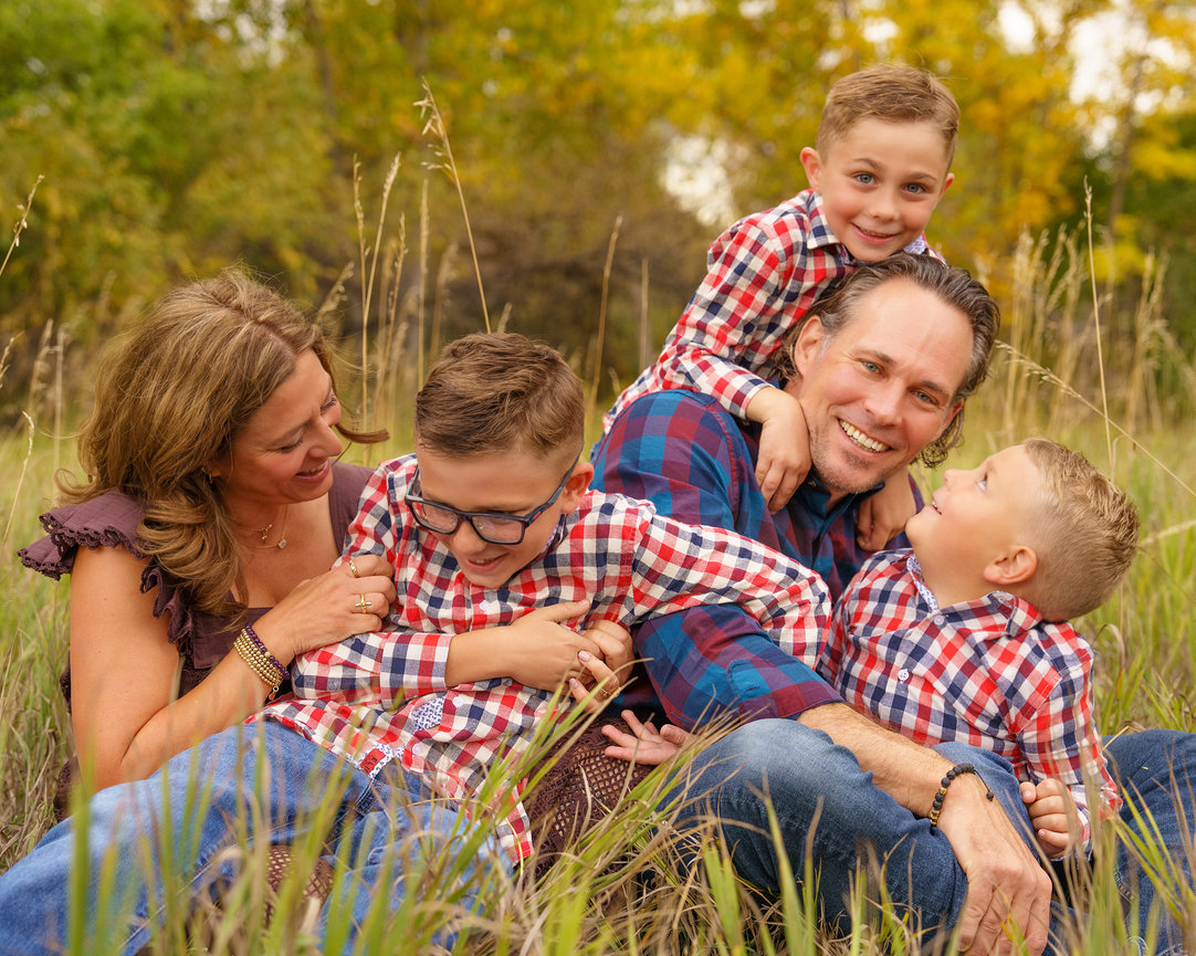 A family of five in plaid shirts sits and plays in a grassy field.