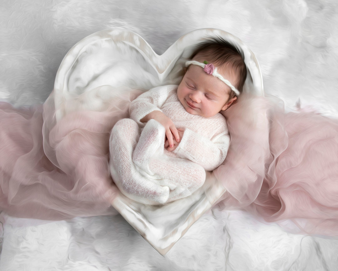 Newborn sleeping in a heart-shaped bowl with pink fabric