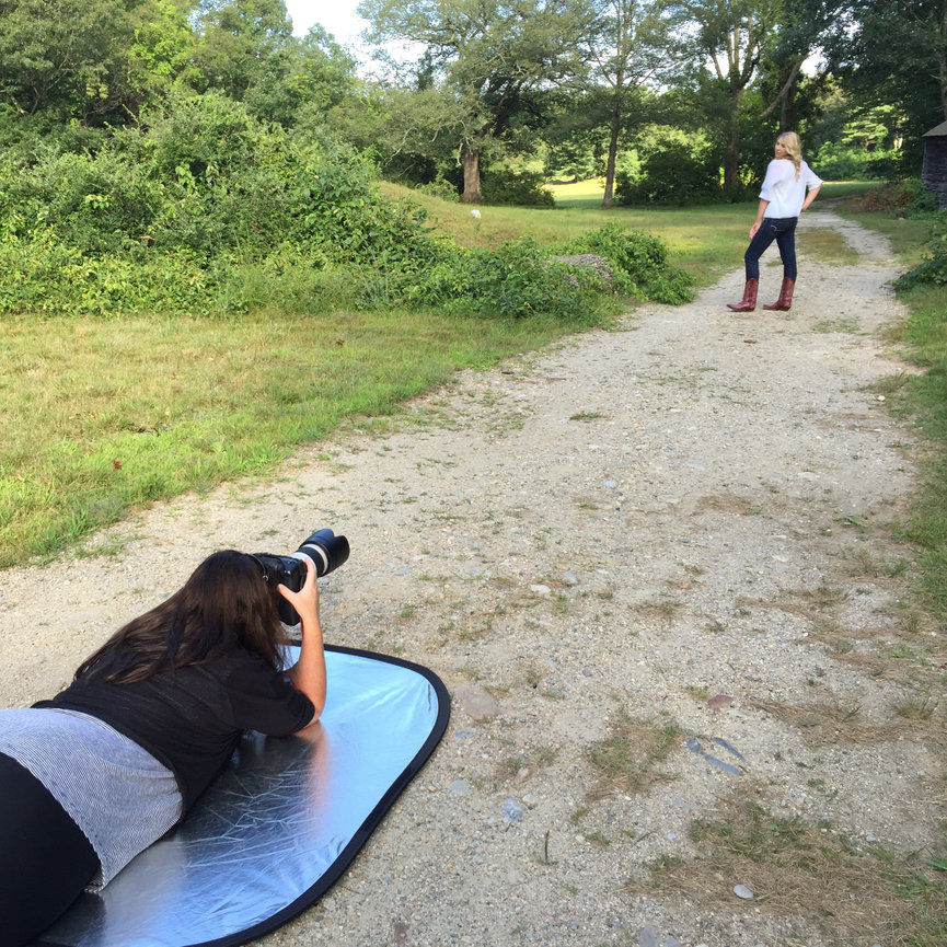 A Paula Swift, photographer lying on a reflectoer as she takes photos of a high school senior in  Sudbury on a path surrounded by greenery.