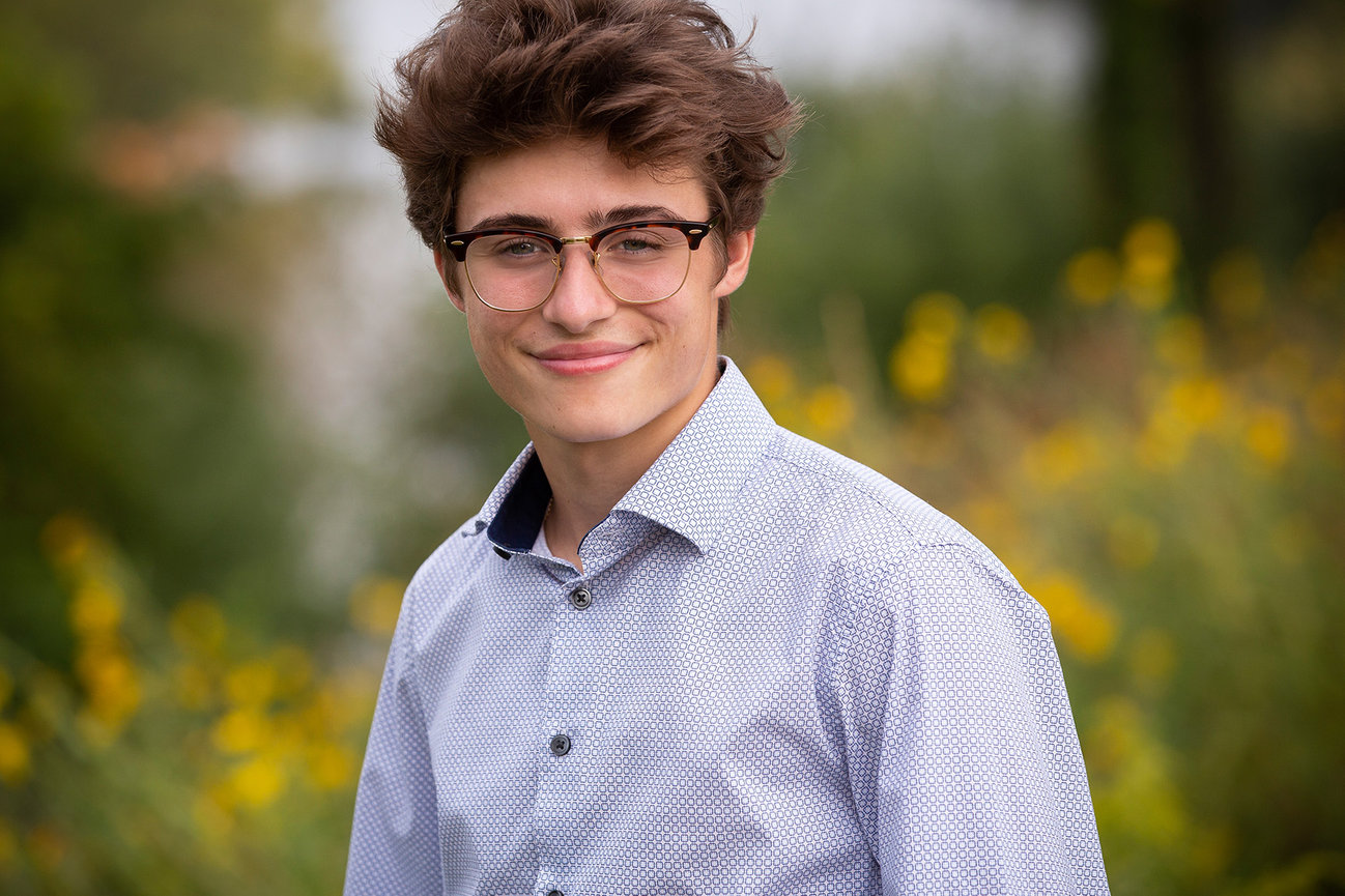 A high school senior boy with glasses and yellow wildflowers blurred out in the background.