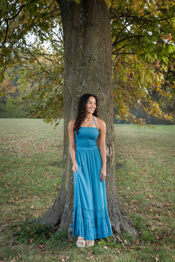 Woman in a blue dress leaning against a tree