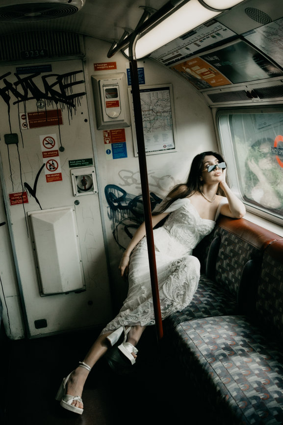 Editorial wedding photography in London: a bride gazing out the window of a graffiti-covered Underground train seat.