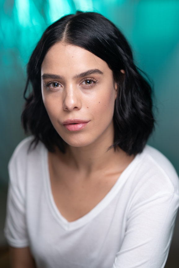 Close-up portrait of a woman with short black hair on a teal background.
