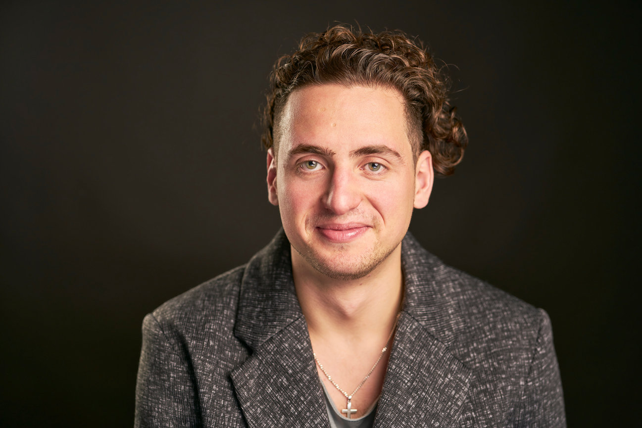 Studio portrait of a smiling young man wearing a textured blazer.