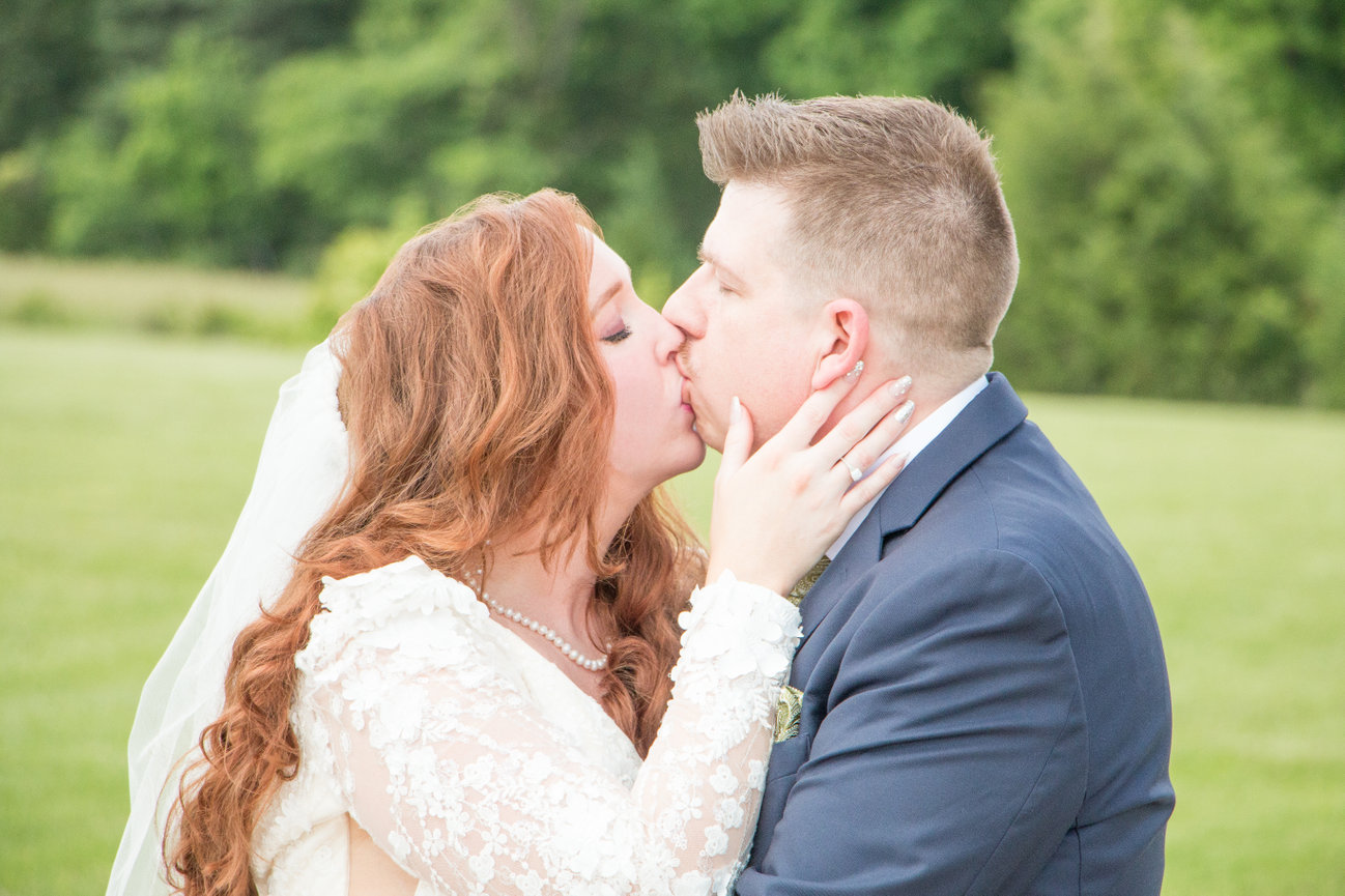 Bride and groom sharing a kiss outdoors, with greenery in the background.