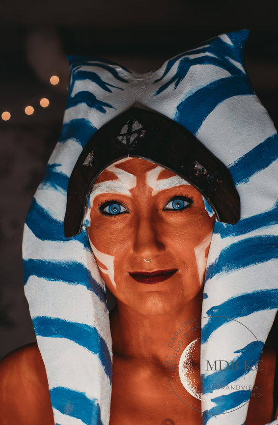 Person dressed as a character with blue and white headpiece, orange face paint, and bright blue eyes.