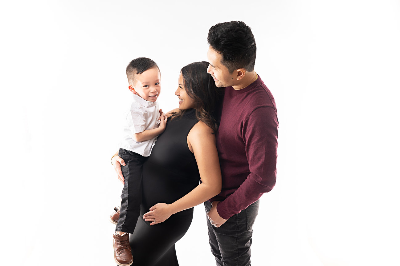 Timeless studio pregnancy portrait of glowing mother surrounded by loving husband and toddler son in elegant poses