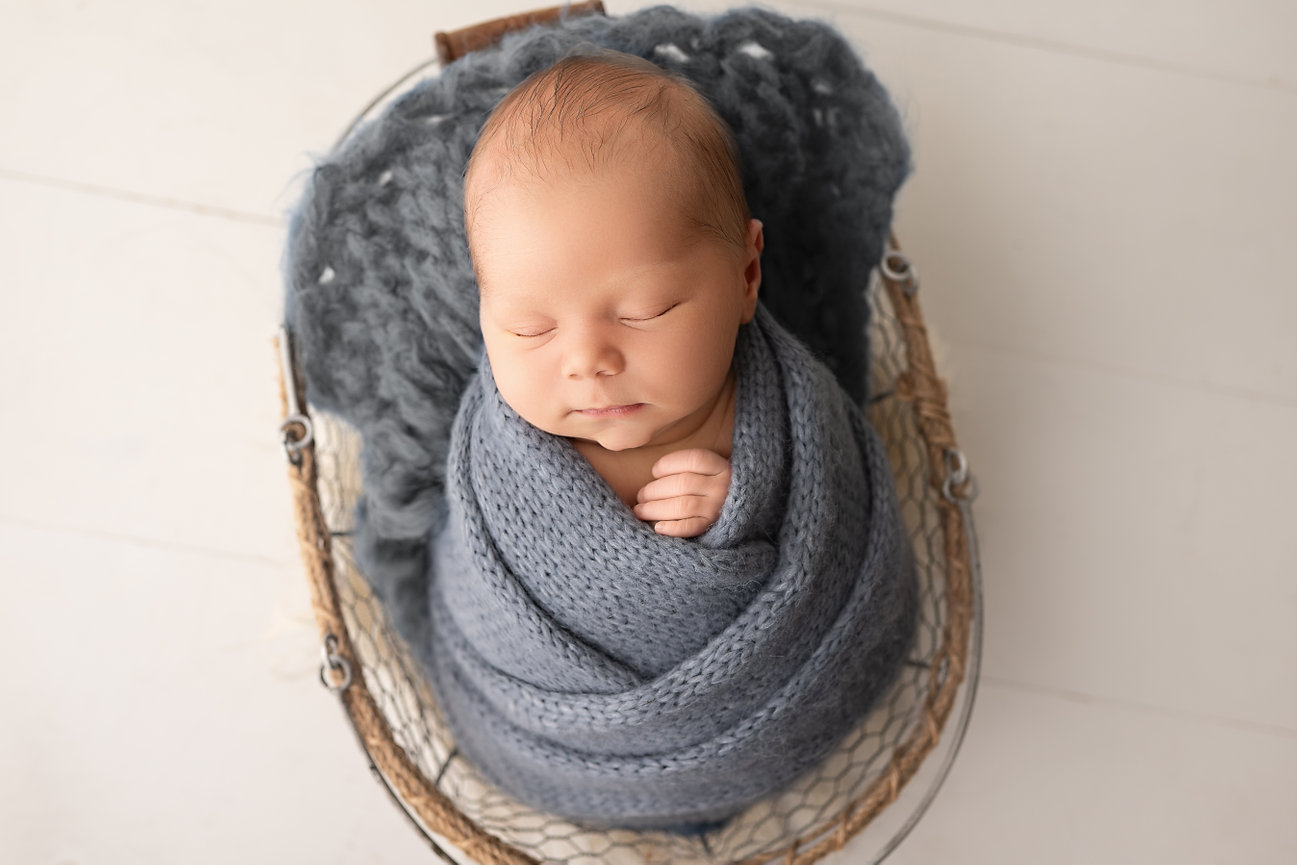 Timeless newborn portrait with textured wrap and prop styling in crate on light wood floor in NJ photography studio