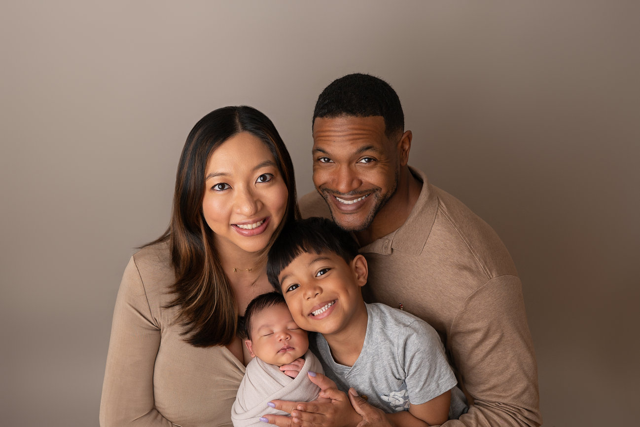 Studio newborn session with older sibling, mom, and dad embracing new baby in a timeless, clean family portrait