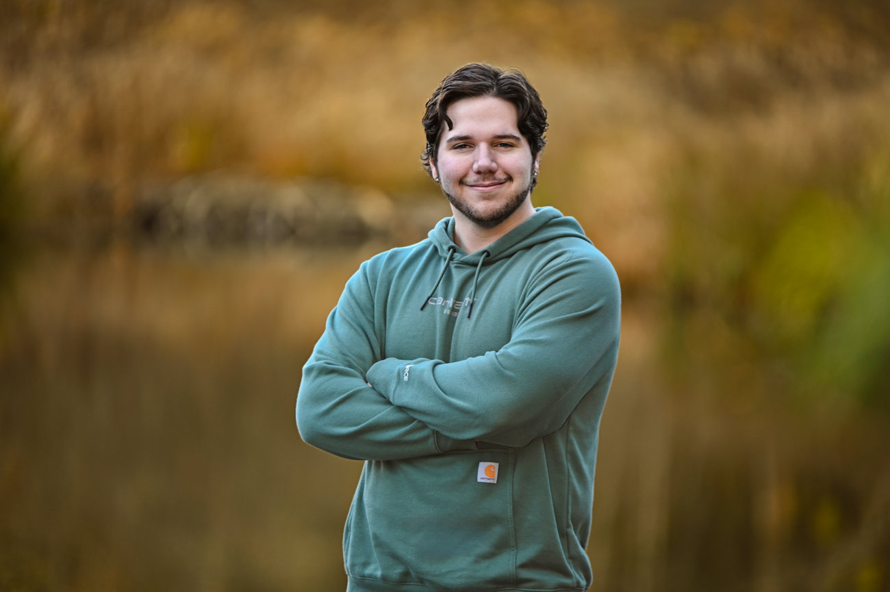 Man standing with arms crossed in a soft-focus outdoor portrait.