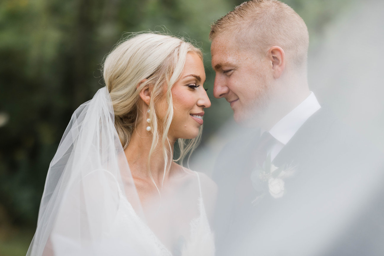 Blonde bride and groom having intimate moments behind veil.