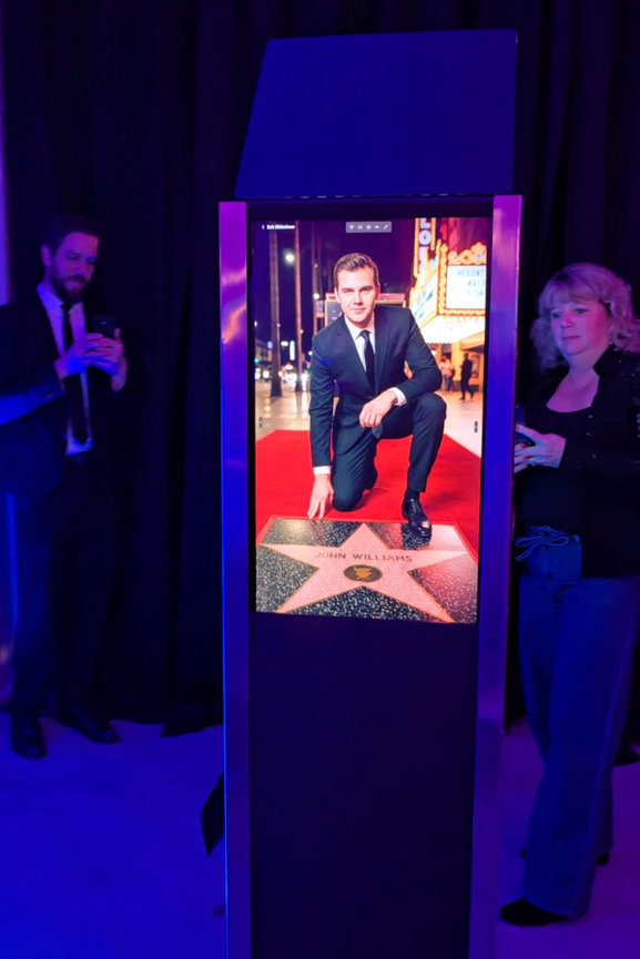 AI photo booth showing a full-color stylized portrait of a guest on the rear vertical display.