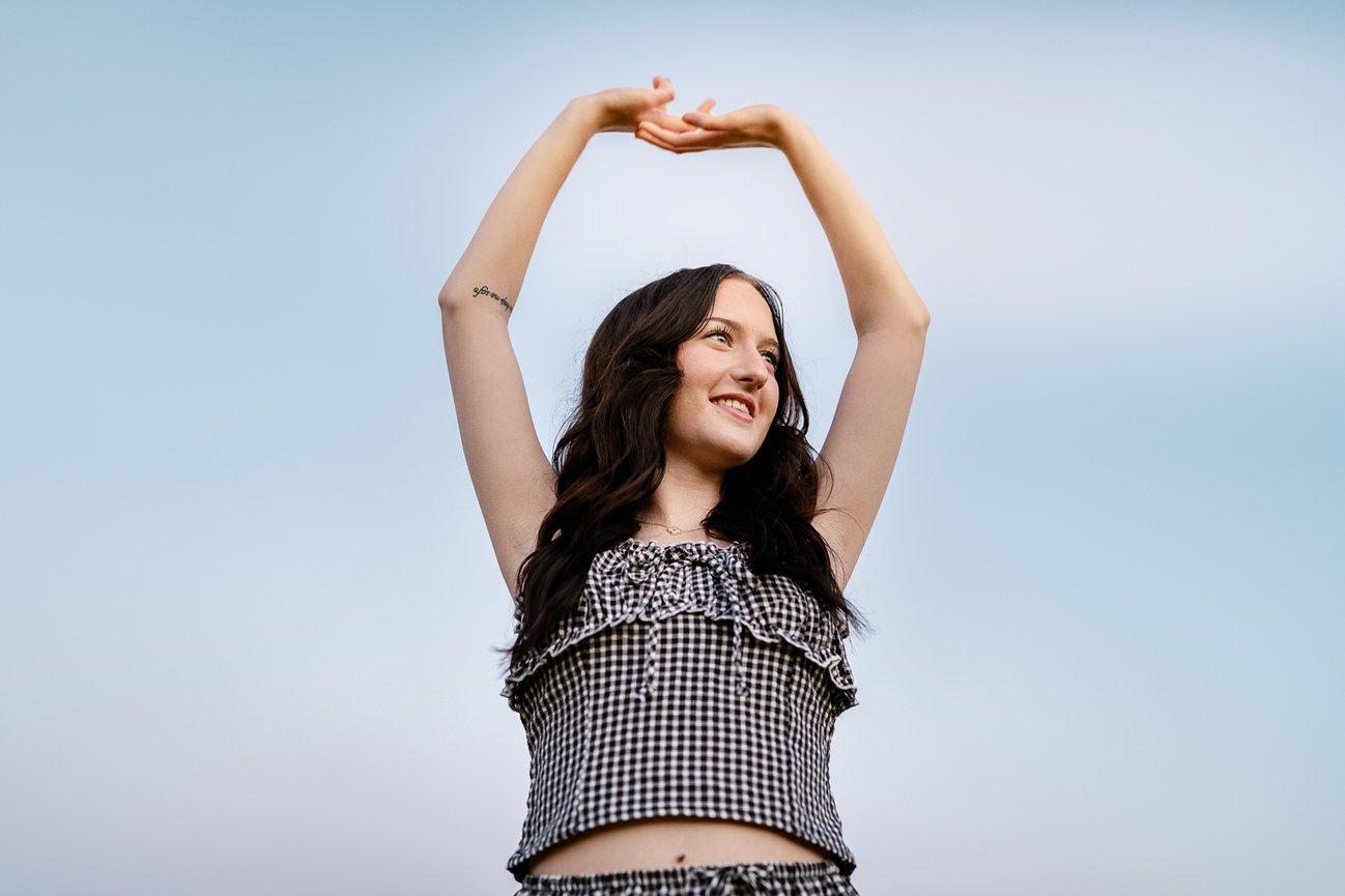 Woman stretching arms upwards under a blue sky