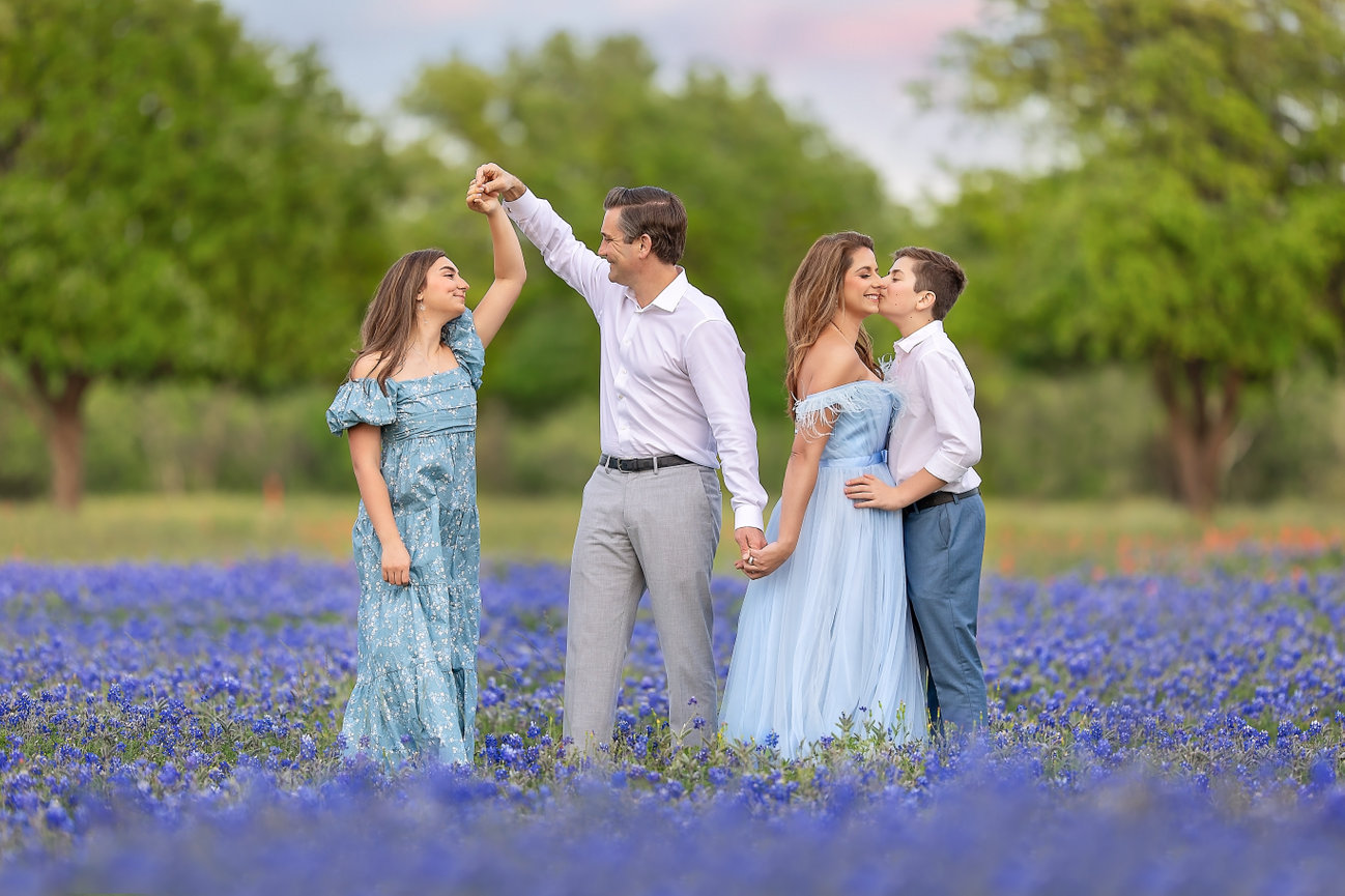 Family of four standing in a blue flower field and pointing at the sky