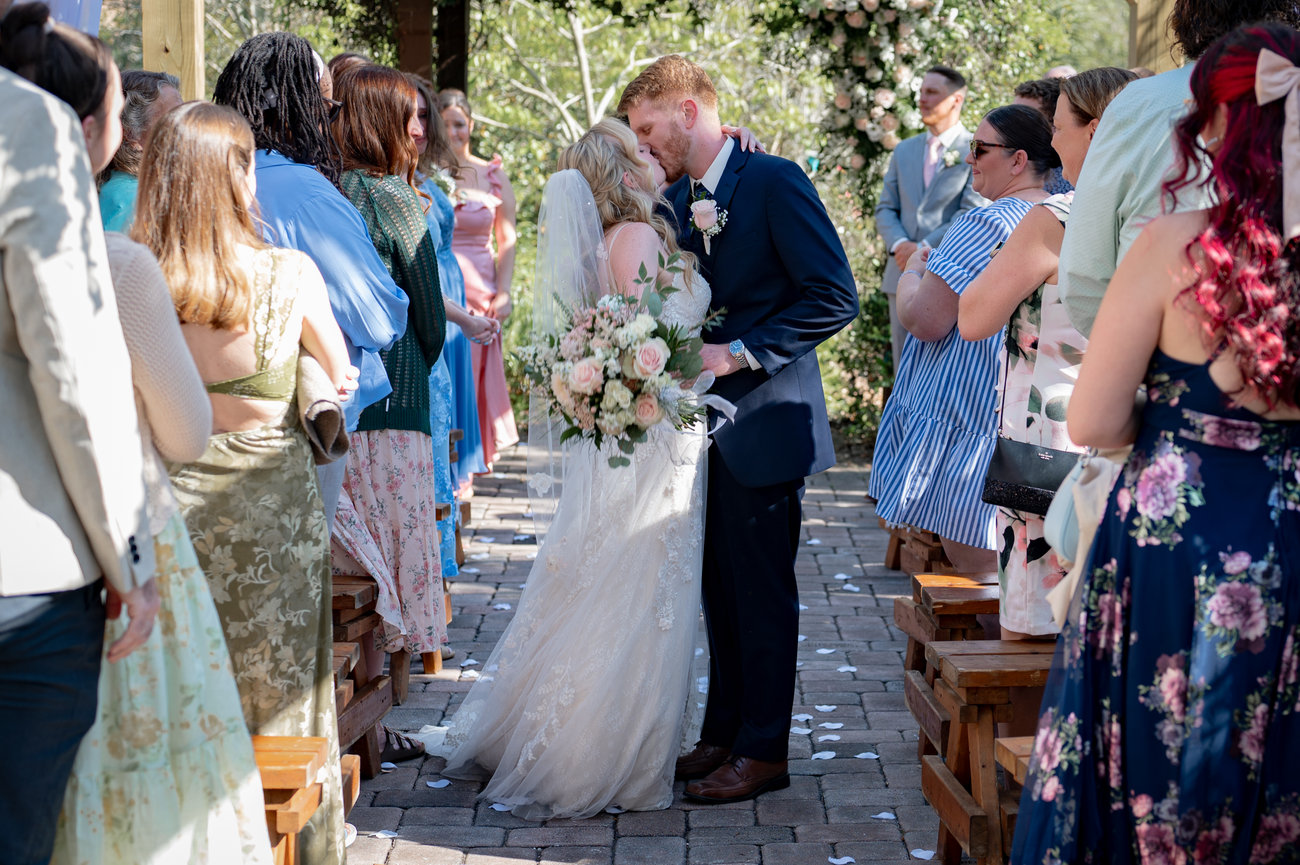 Bride and groom kissing at a wedding reception surrounded by guests.