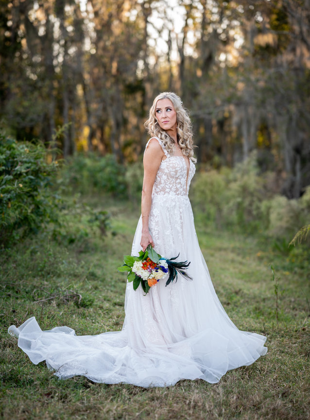 Bride in a long white wedding gown standing outdoors with a bouquet.