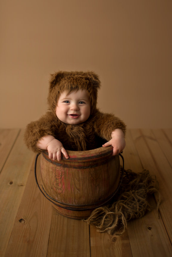 6 month old baby boy in a furry bear outfit smiling in a wooden bucket during milestone photoshoot with Kansas City Kansas baby photographer Dreamworks Photography 