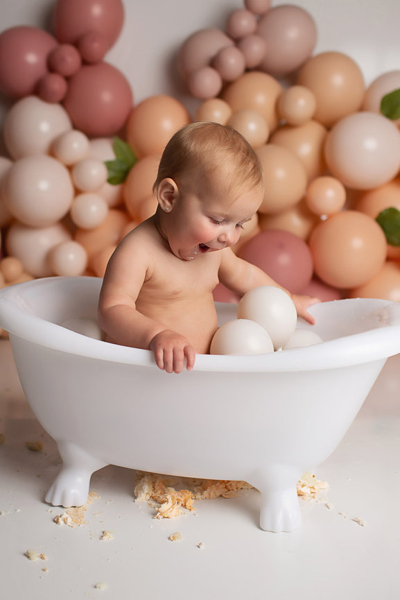 happy baby girl splashing in tub playing with balloons during Kansas City cake smash first birthday photography session with baby photographer Dreamworks Photography in Kansas City photography studio