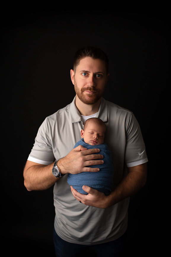 Newborn baby boy wrapped in blue fabric being held by his dad during newborn photoshoot with newborn photographer Dreamworks Photography in Kansas City 