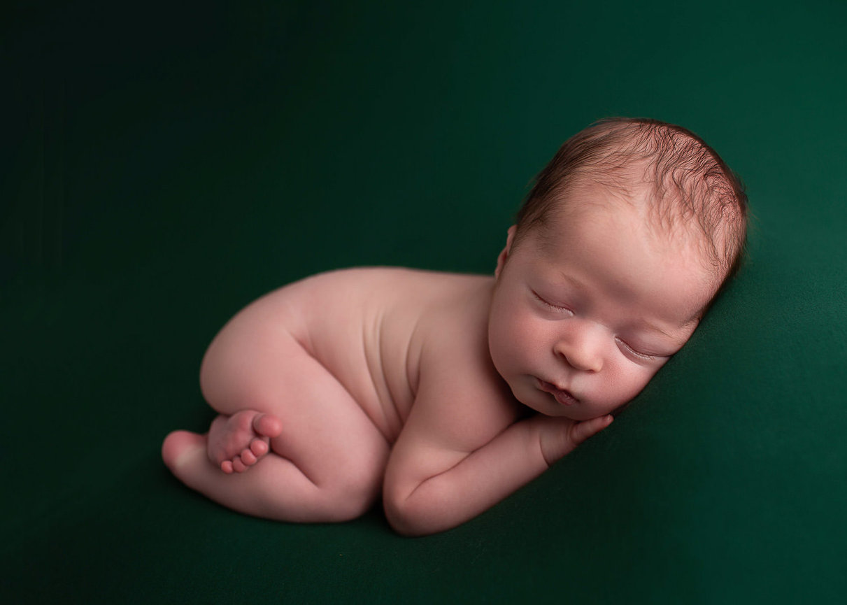 Newborn baby boy sleeping in bum up pose on green backdrop during newborn photo session with newborn photographer Dreamworks Photography in Kansas City newborn photography studio