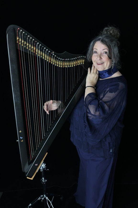 Woman in a blue dress posing beside a black harp on a dark background. Business content photos melb