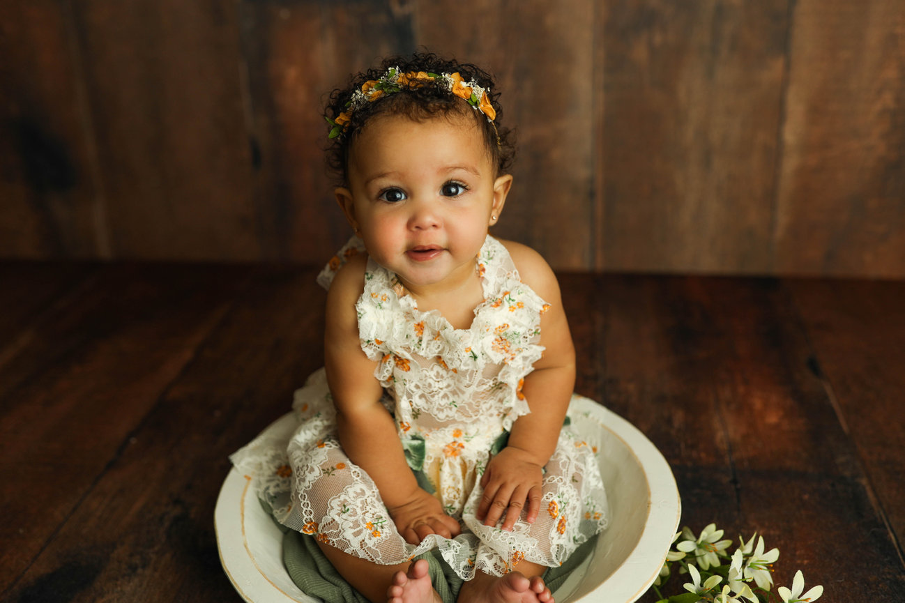 milestone baby portrait photo session sitting and smiling in round ceramic with floral dress and headband