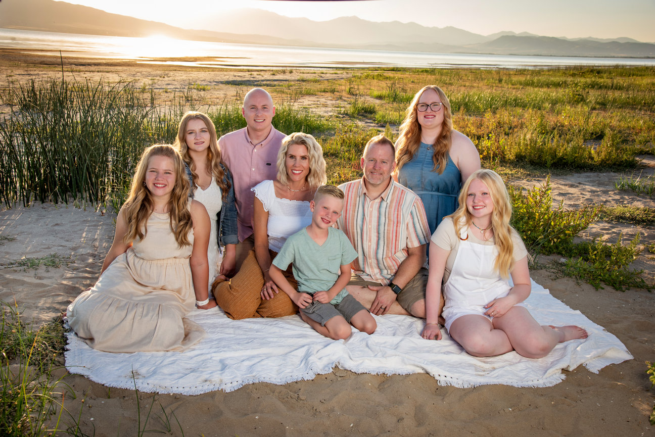 A family sitting on a blanket at the edge of a beautiful lake at sunset.
