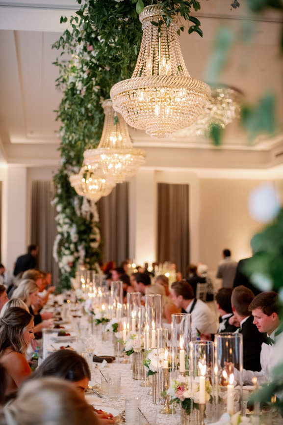 Head table at seated dinner reception glowing with candles and hanging florals. Wedding photography by Heather Durham.