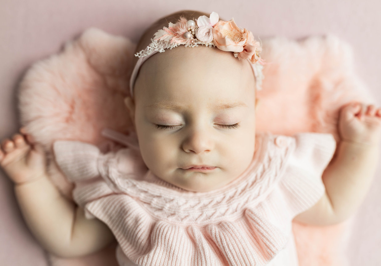 sleeping baby with plush pink backdrop in pink clothes and headband