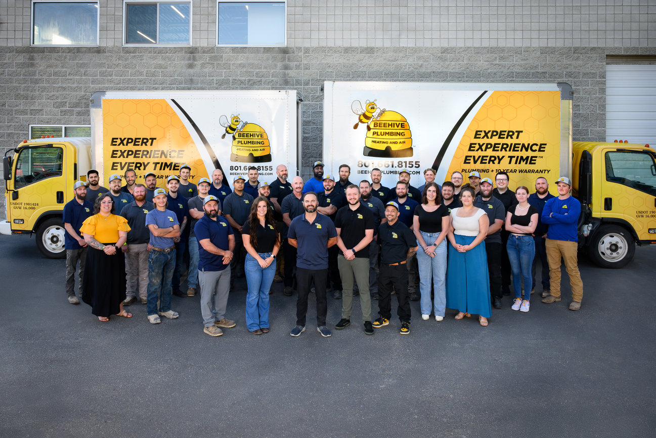 Group photo of BeeHive Plumbing team in front of two branded trucks, showcasing staff in uniforms.