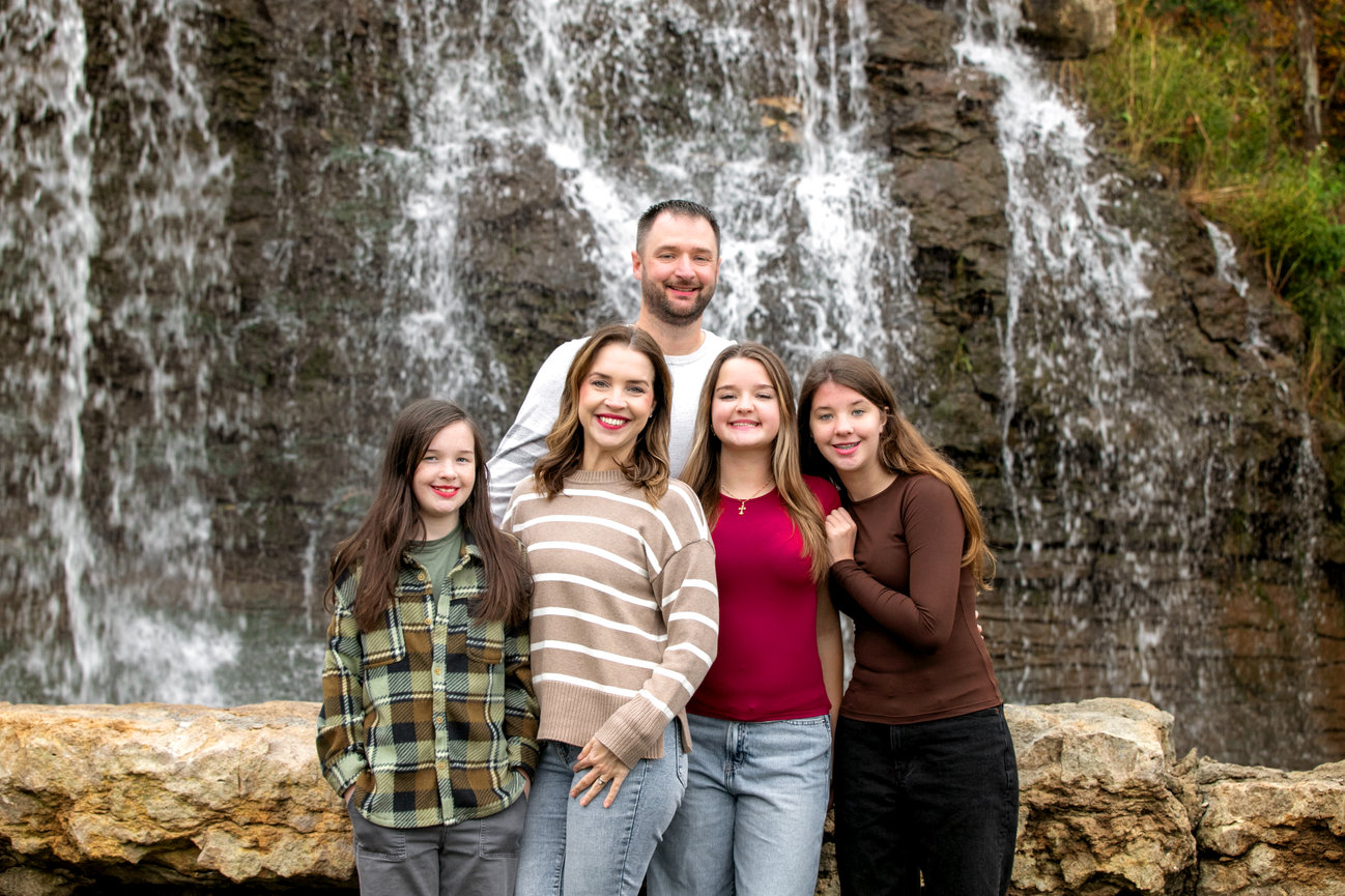 Family of five posing in front of a waterfall outdoors
