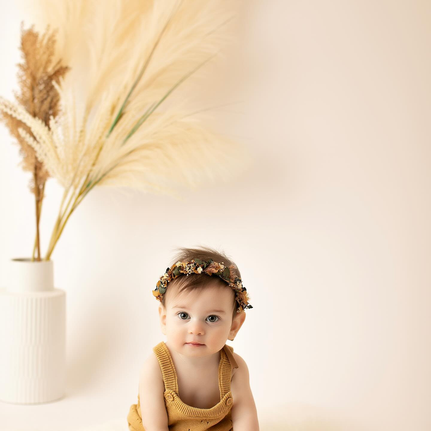 Baby in a mustard outfit sitting beside pampas grass