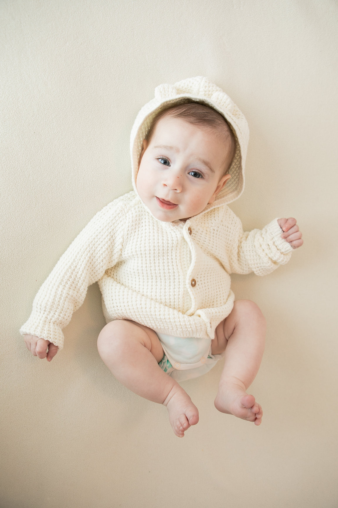 Baby lying on a beige backdrop in a cream knitted outfit