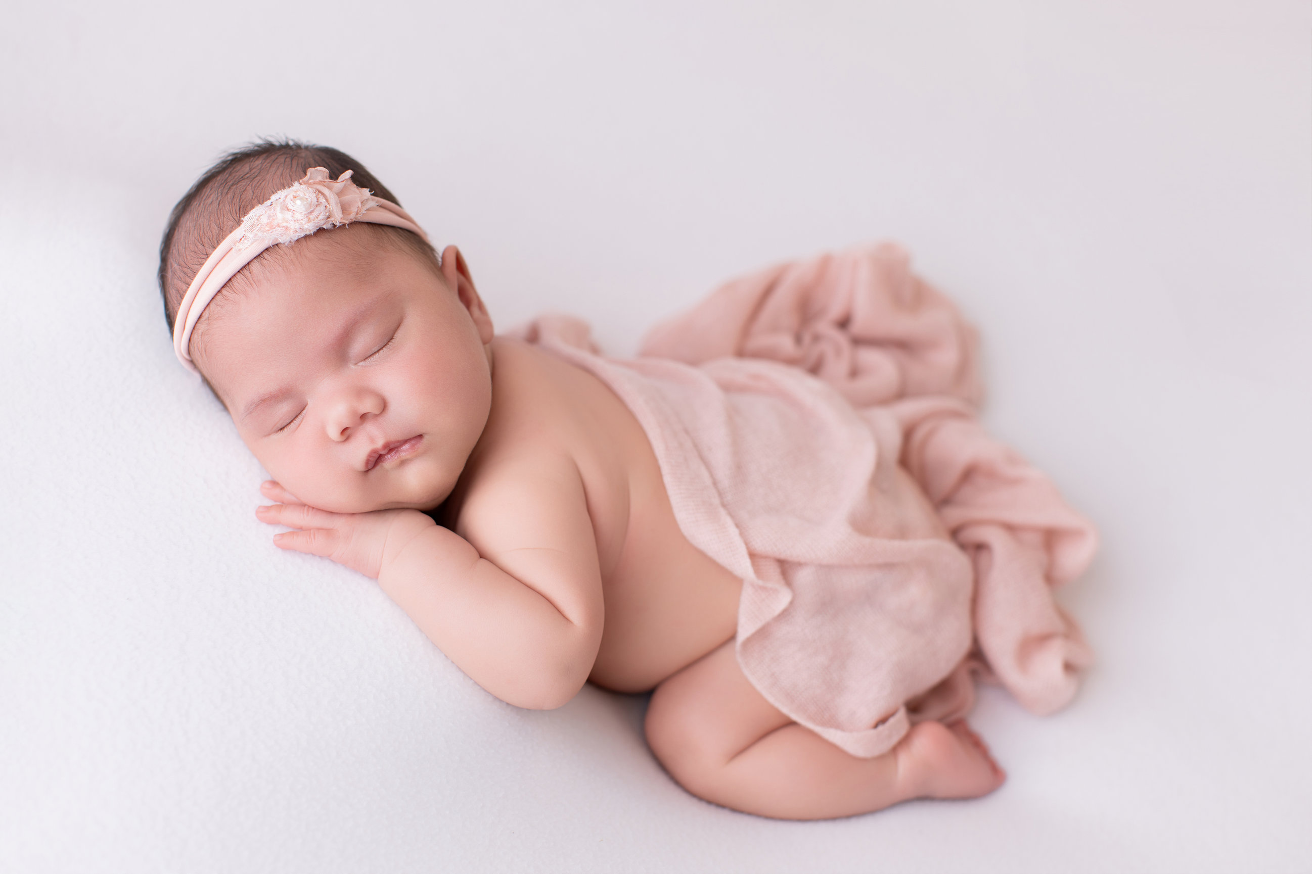 Newborn baby girl asleep in a blush pink wrap on a white backdrop, Calgary newborn photography