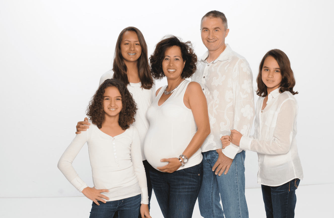 A family standing together with an expectant mother, her husband, and their three teenage daughters at Kliks Photography.