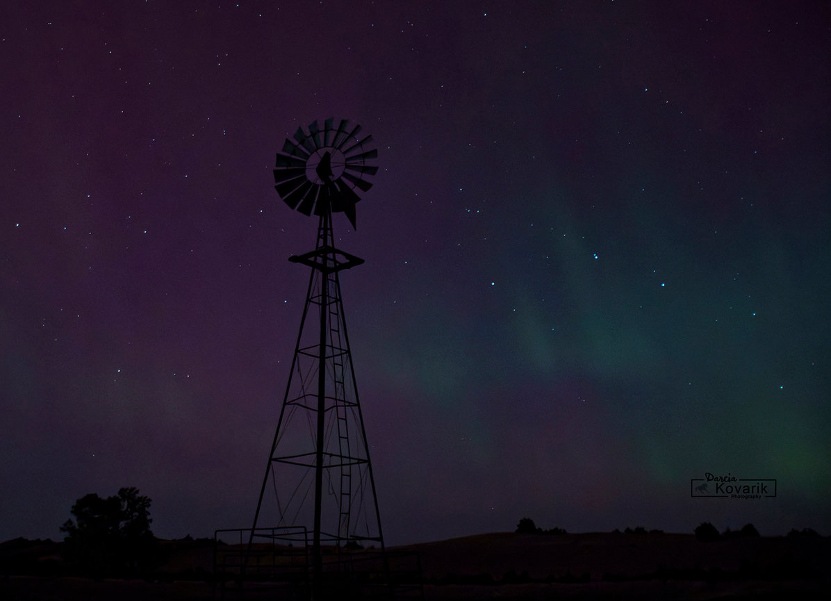 Silhouetted windmill against a starry sky lit by the northern lights.