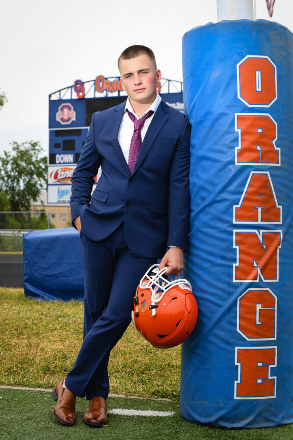 Teenage boy football player wearing a suit and holding his football helmet for senior pictures in Dublin OH.