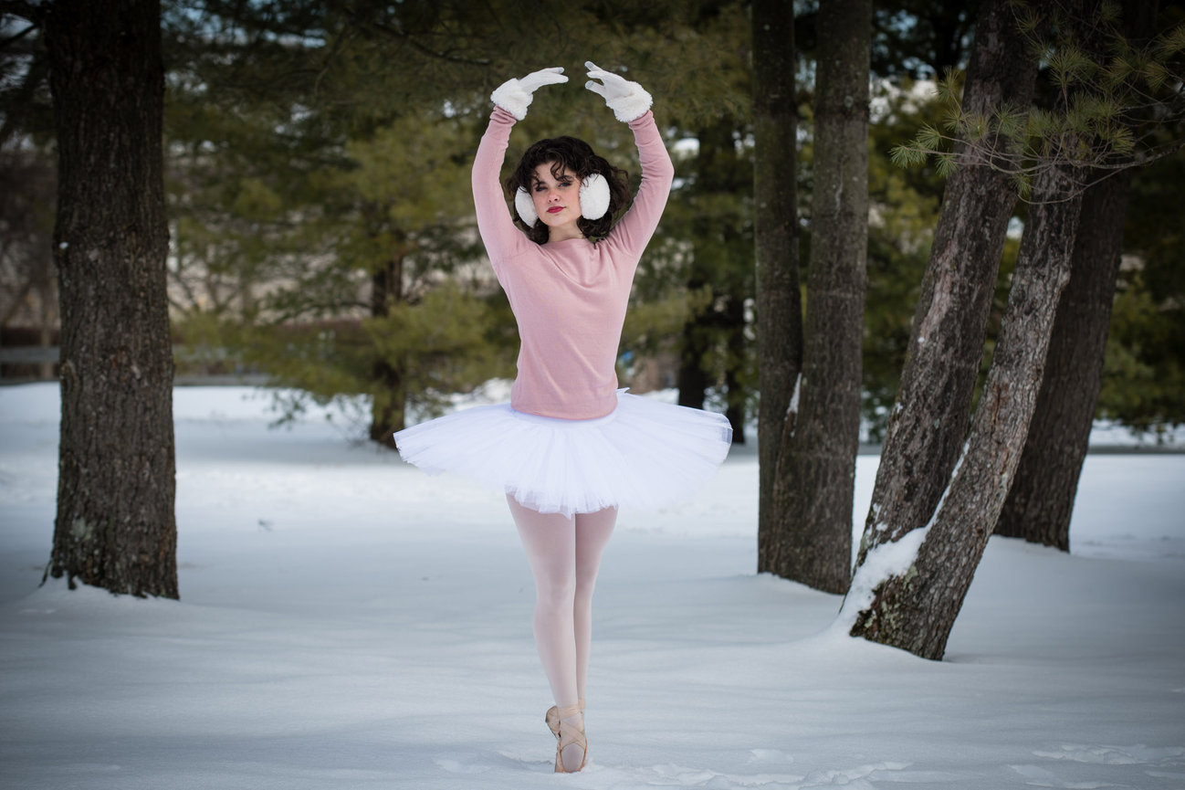 Ballet dancer in pink attire and white tutu performing an arabesque in a snowy forest setting.